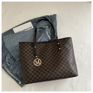 Detail of monogram tote bag with gold M pendant on textured background with casual props