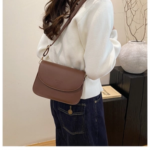 Sac bandoulière en cuir mat marron porté par un mannequin dans un cadre minimaliste