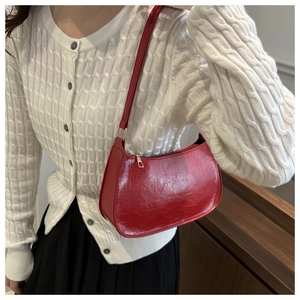 Close-up of red oil-wax leather crescent bag worn with a white cable-knit sweater