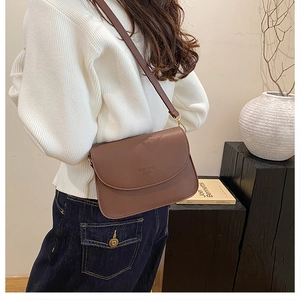 Gros plan d'un sac bandoulière en cuir marron avec texte FASHION BAGS sur pull blanc