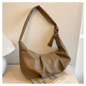 Detail of coffee brown pleated dumpling bag with knotted strap on a minimalist desk