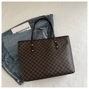 Detail of large brown tote bag showing repetitive M pattern and gold rivet accents