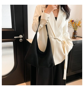 Borsa hobo nera minimalista con finitura opaca indossata da una modella in abito bianco