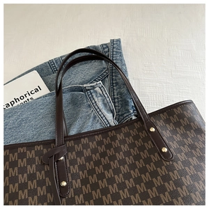 Close-up of brown monogram tote bag with leather straps and rivet detail in a stylish setting