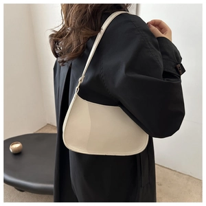 Model wearing a cream patent leather underarm bag with glossy finish for daily commute