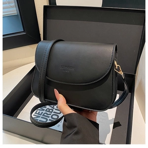 Détail du sac bandoulière en cuir noir avec logo gravé et attaches en forme de cœur doré