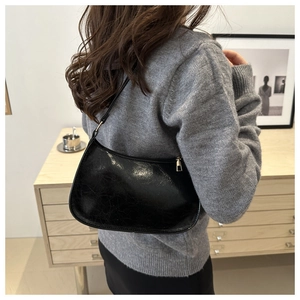 Close-up of black patent leather hobo bag with vintage texture on a model's shoulder