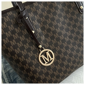 Detailed macro view of dark brown tote bag texture and golden M-logo metal pendant