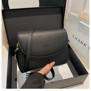 Gros plan sur un sac bandoulière en cuir noir mat avec logo embossé et boîte cadeau