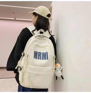 Detailed back view of a cream white student backpack with blue MRMI logo and duck charm