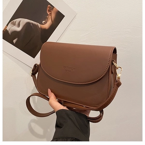 Détail de la texture du cuir marron et de la boucle en métal doré sur le petit sac bandoulière