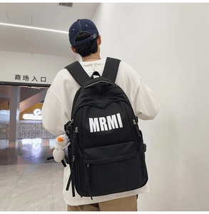 Detail of black nylon backpack with white MRMI letters and cute duck plush pendant