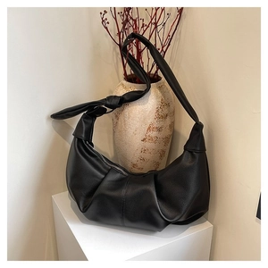 Detail of black pleated croissant bag featuring litchi grain texture and knotted strap