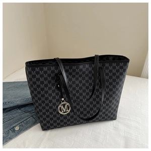 Detail of grey tote bag with M-letter pattern, leather handles, and metal charm