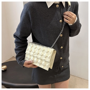 Detail of a creamy white quilted shoulder bag with silver chain strap and metal clasp