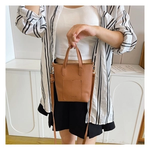 Detail of a brown lychee pattern leather shoulder bag with a fashion logo and adjustable strap