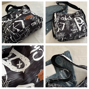 Close-up of black canvas bag with white graffiti patterns and a brown leather logo tag