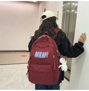 Macro detail of wine red backpack with MRMI logo and cute white duck pendant