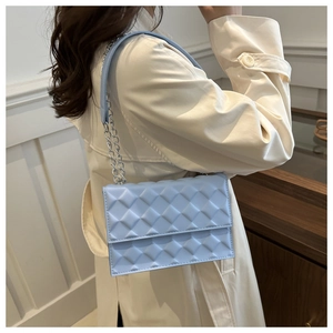 Detail of light blue quilted diamond pattern shoulder bag with silver chain strap worn by model