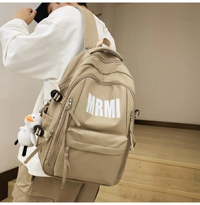 Detail of khaki minimalist backpack featuring multiple zipper pockets and duck pendant