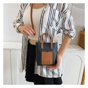 Detail of a mini two-tone crossbody bag in black litchi grain with brown front pocket