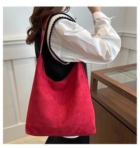 Detail view of large red suede tote bag with wide shoulder strap worn by a model