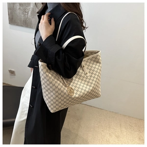 Detail of elegant beige tote bag with M-letter monogram print and gold metallic charm