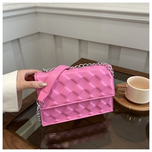 Detail view of pink quilted shoulder bag with silver chain strap on a wooden table