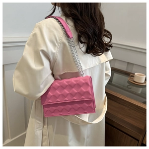 Pink quilted shoulder bag with silver chain strap shown from a side view on a beige coat