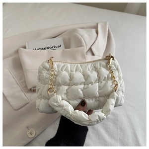 Detail of white quilted dumpling bag with gold chain strap on a soft white bed