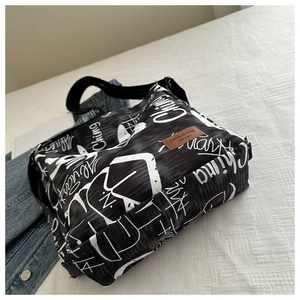 Detail of canvas crossbody bag with white graffiti pattern and brown fashion leather patch