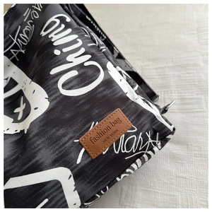Close-up of black and white graffiti canvas fabric with a leather logo label on the bag
