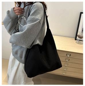 Detail shot of a large black suede tote bag shown on a shoulder in a minimalist setting