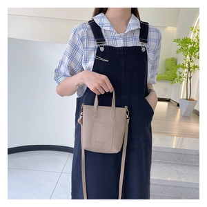 Detail view of beige pebbled leather mini crossbody bag with embossed fashion logo text