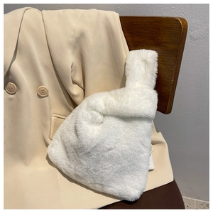 Close-up of white plush faux fur handbag on a wooden chair with a beige blazer background