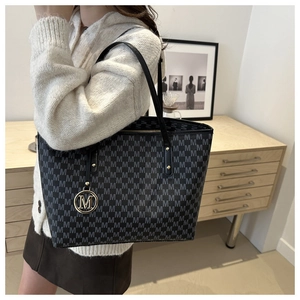 Detail of black tote bag with M letter monogram print and gold metal pendant decoration