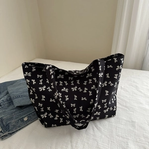Detailed shot of large black tote bag with white bow prints on soft white bedding