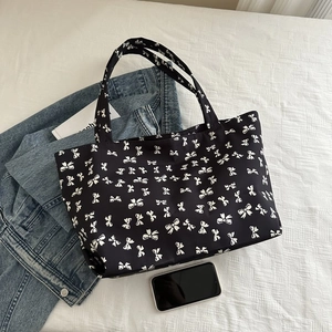 Close-up of black tote bag with white bow print and durable dual handle detail