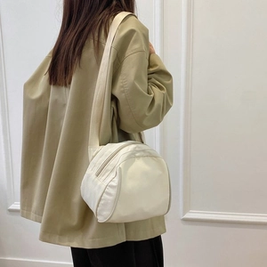 Adjustable wide strap detail on cream-white canvas crossbody bag worn with khaki shirt