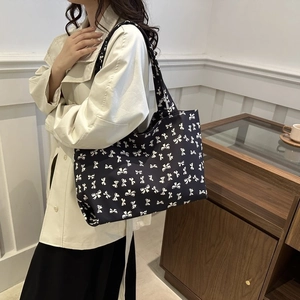 Detail of a large black tote bag with white bow print and comfortable wide shoulder strap