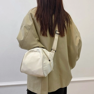 Minimalist beige crossbody bag shown on model with adjustable strap and curved shape