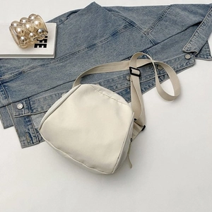 Flat lay of off-white canvas crossbody bag with adjustable strap on a denim jacket
