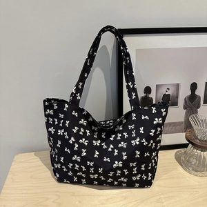 Detail of a large black tote bag featuring white bow patterns on a light wooden table