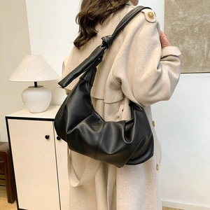Detail of a black matte leather croissant bag with knotted strap and pleated design