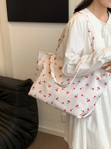 Détail d'un grand sac cabas blanc à motif cerise porté par un mannequin à l'épaule