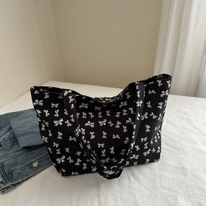 Close-up detail of large black tote bag with white bow pattern and reinforced handles