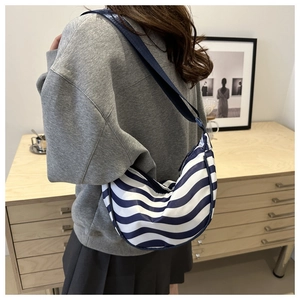 Borsa hobo a righe bianche e blu indossata da modella in una stanza dal design moderno