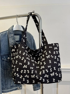 Detail of a black canvas tote bag featuring an all-over white bow pattern print