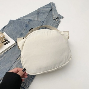 Detailed close-up of cream canvas crossbody bag with adjustable black buckle and strap