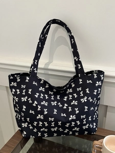 Detail shot of a dark tote bag featuring a white bow pattern on a wooden table